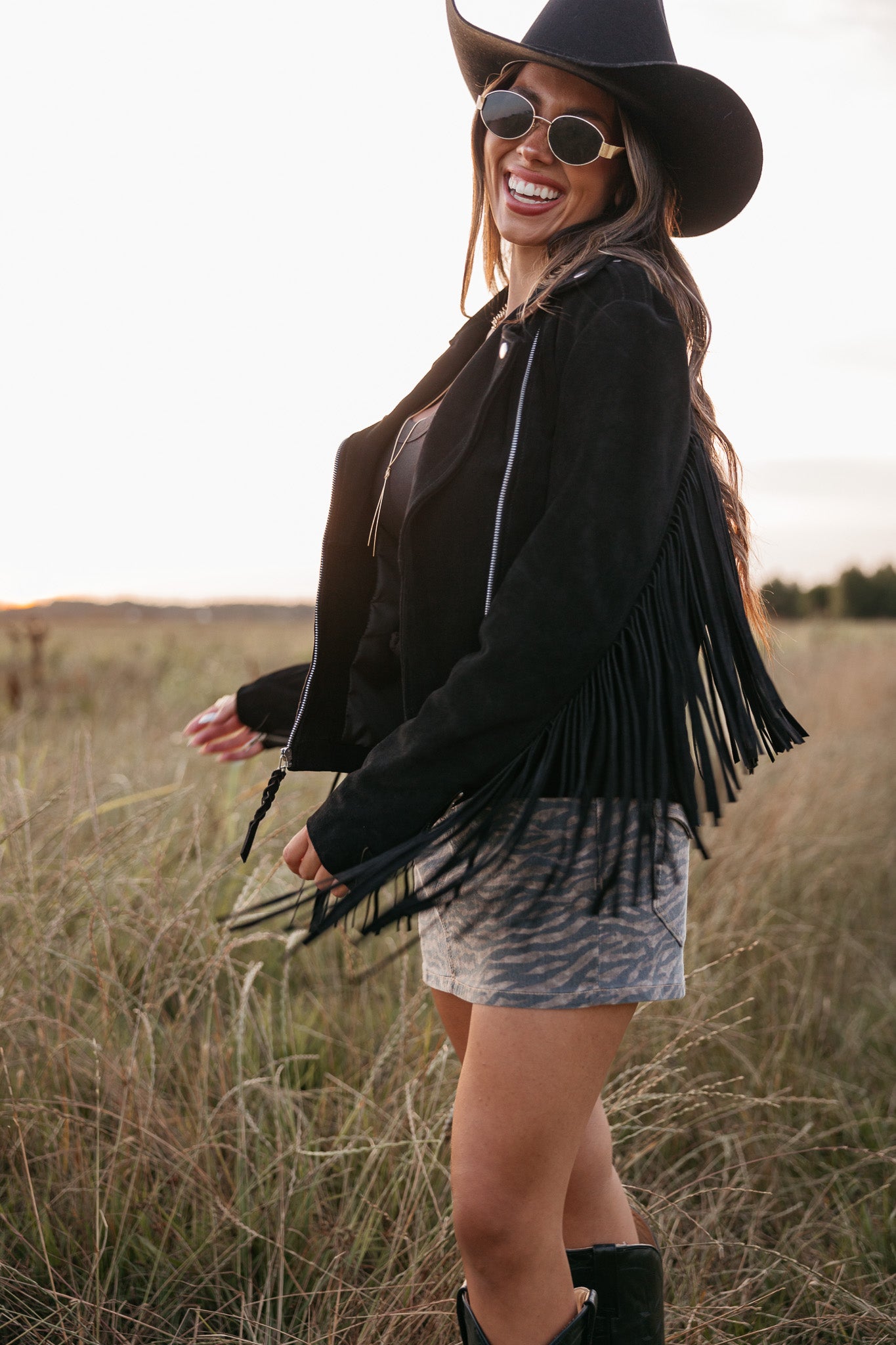 Woman wearing a black fringe jacket and hat in a field