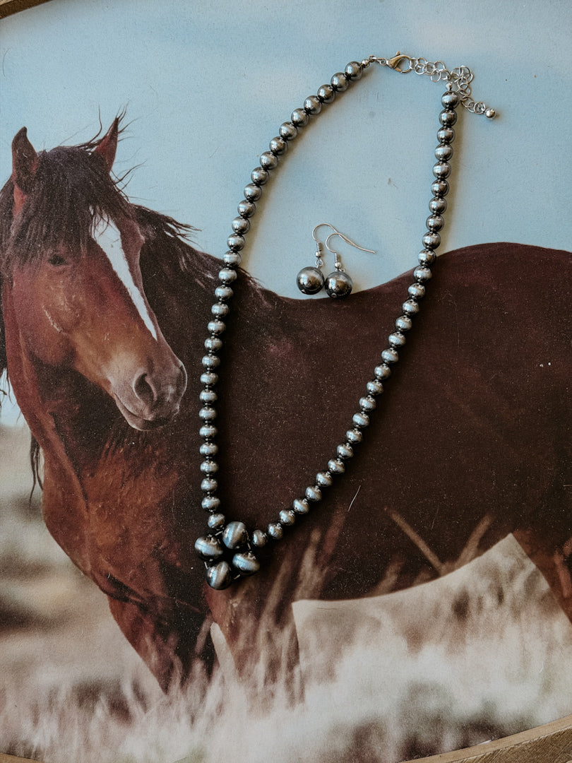 Western beaded necklace and earrings set with floral pendant on horse background