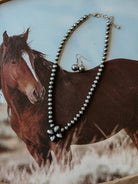 Western beaded necklace and earrings set with floral pendant on horse background