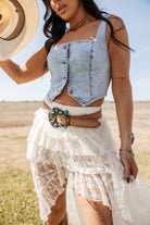 Woman in denim crop top, lace western skirt, and turquoise belt outdoors, boho cowgirl style