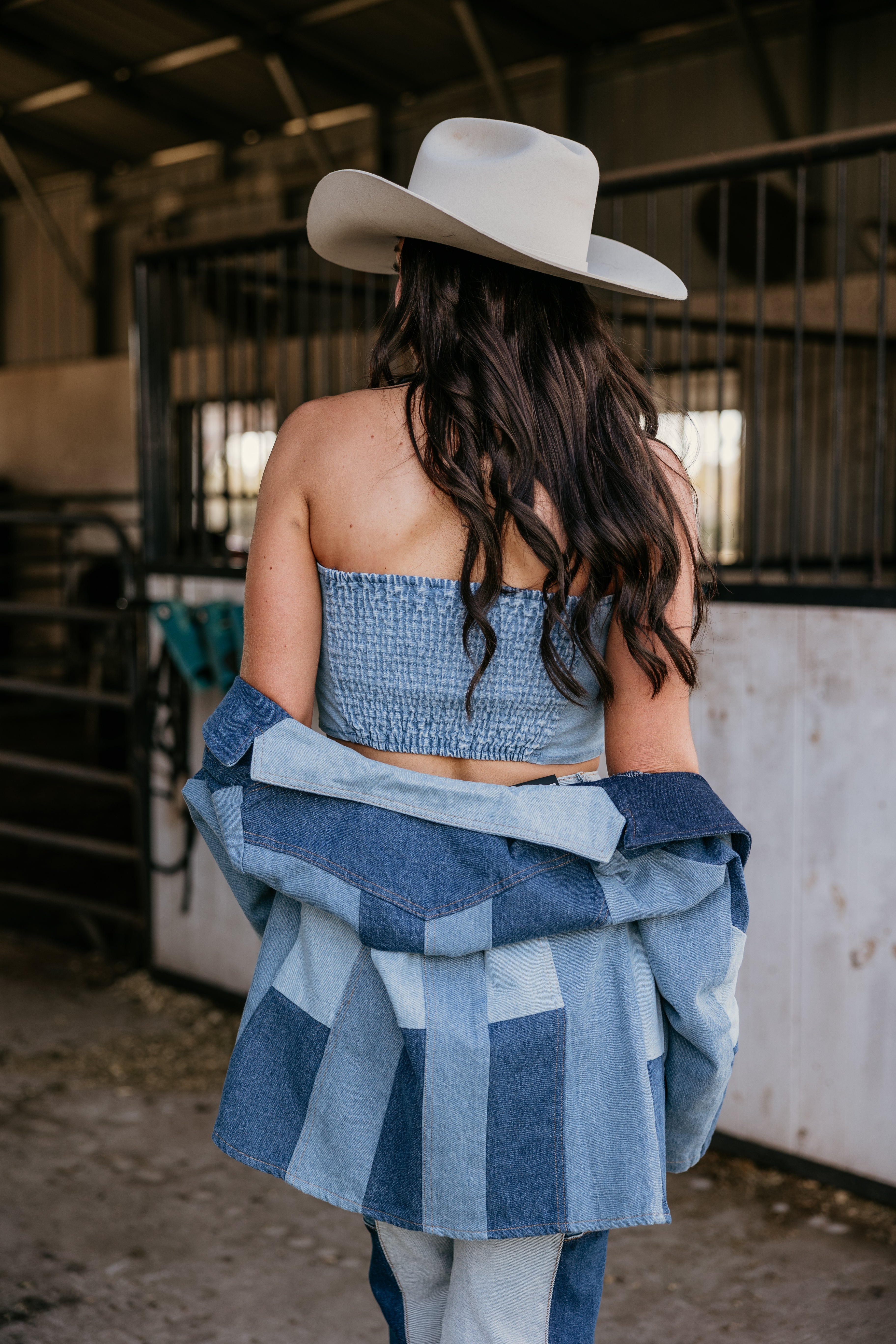 Woman in denim patchwork outfit and cowboy hat, western boho style in barn setting