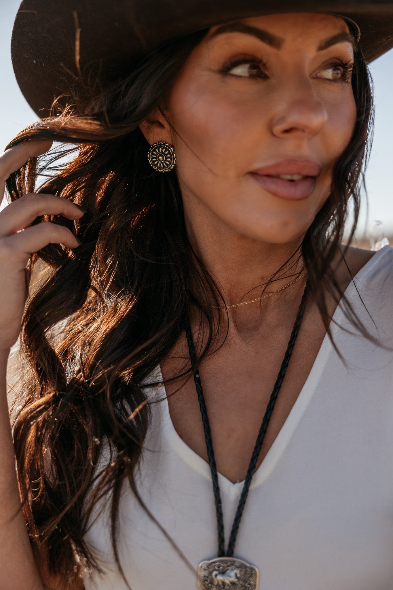 Woman in western boho outfit with concho earrings, black hat, and bolo tie necklace