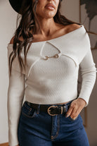 Woman in off-shoulder white knit sweater with gold accent, blue jeans, western belt