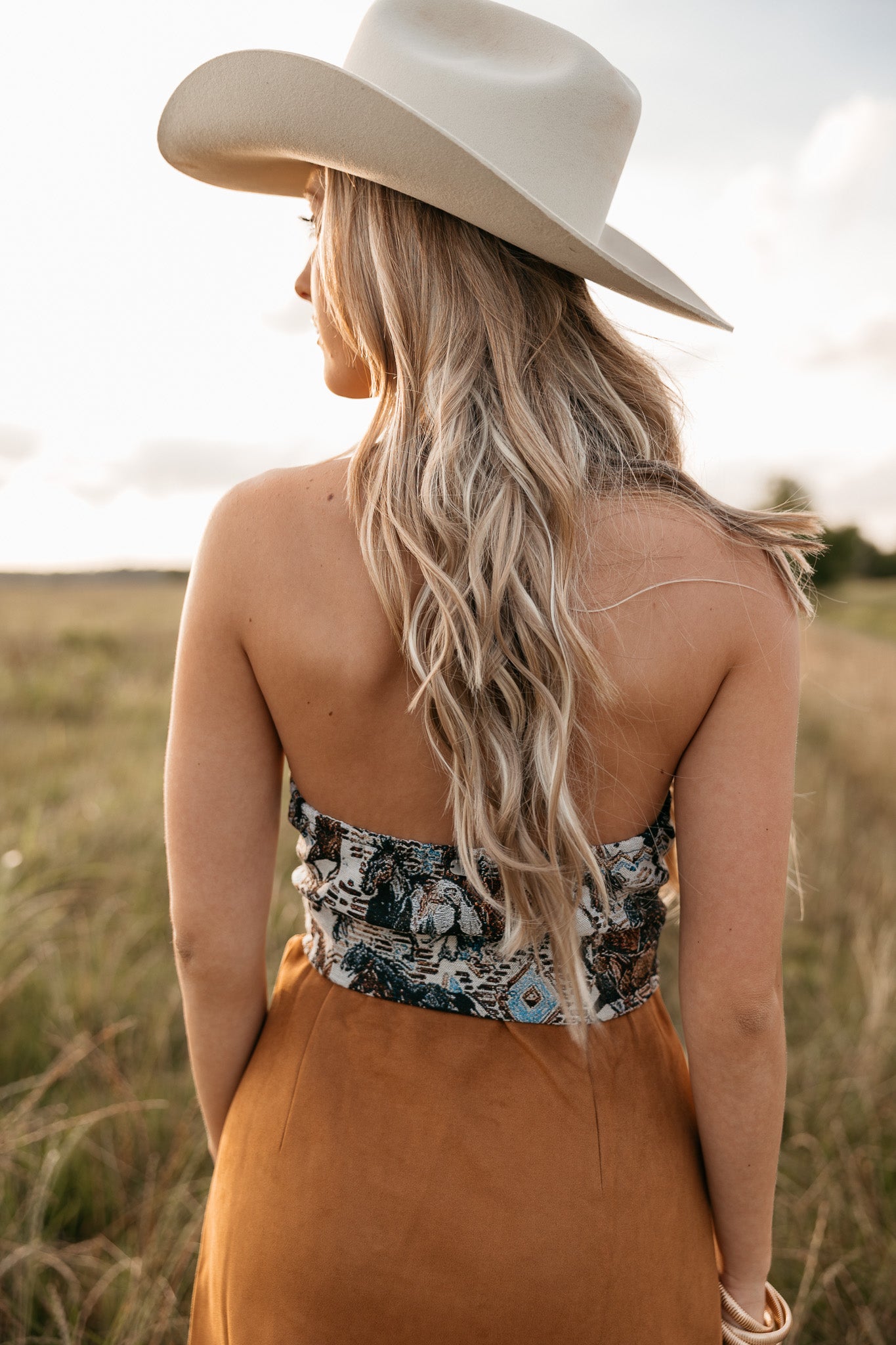 women wearing western halter top with low back and a camel skirt standing in a field. 