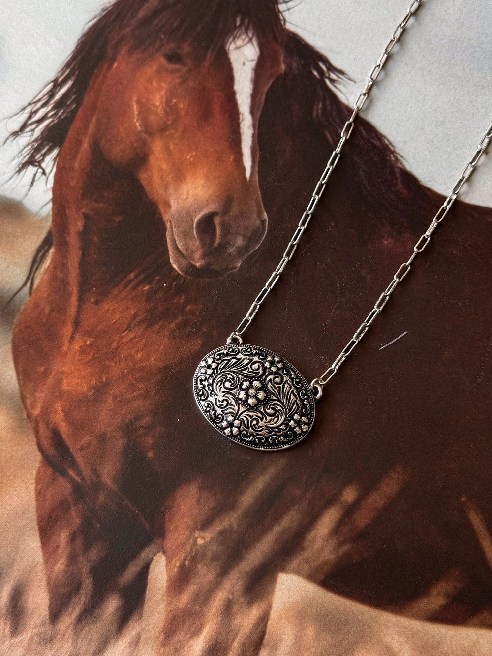 Silver necklace with a decorative pendant in front of a horse painting