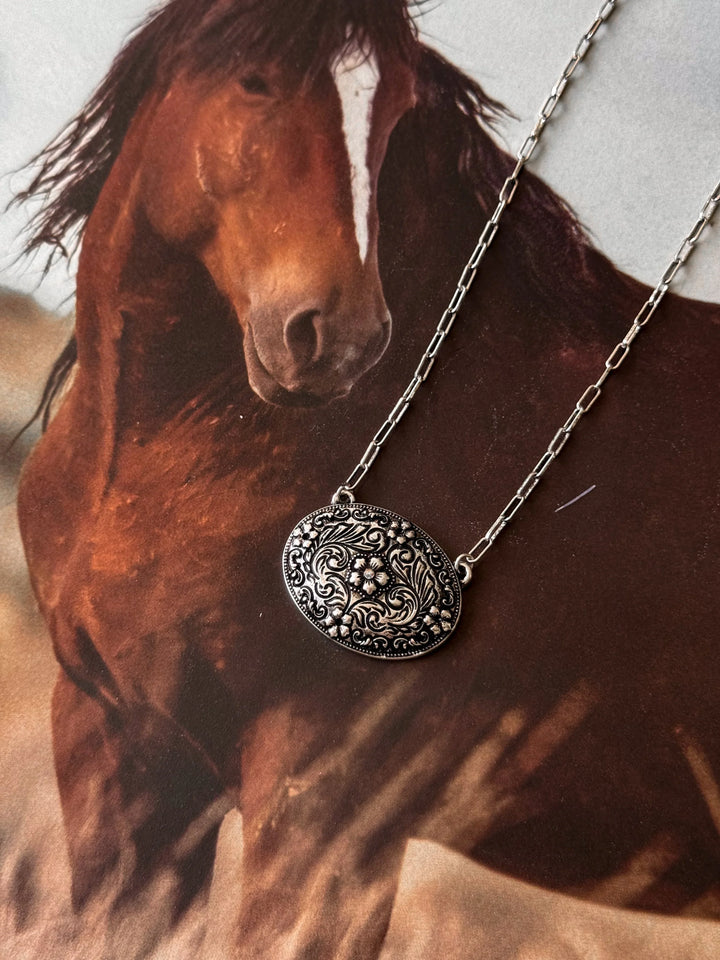 Silver necklace with a decorative pendant in front of a horse painting