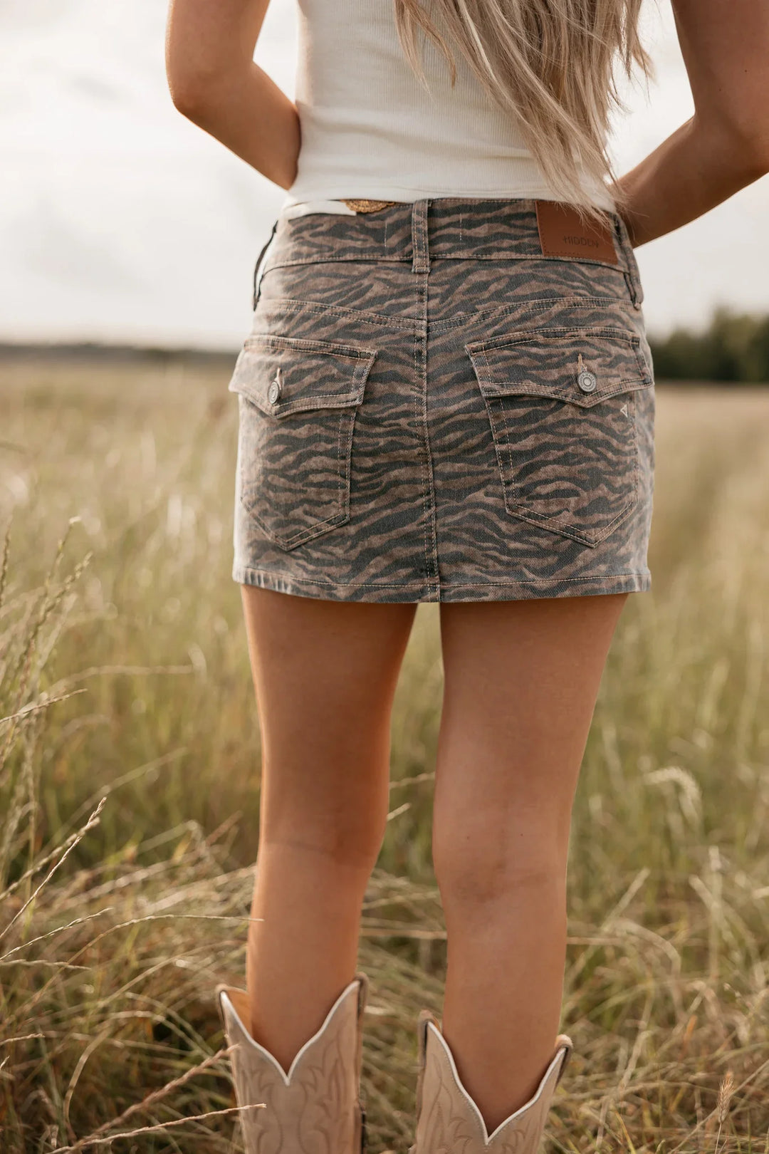 Person wearing a tiger print skirt and cowboy boots in a field