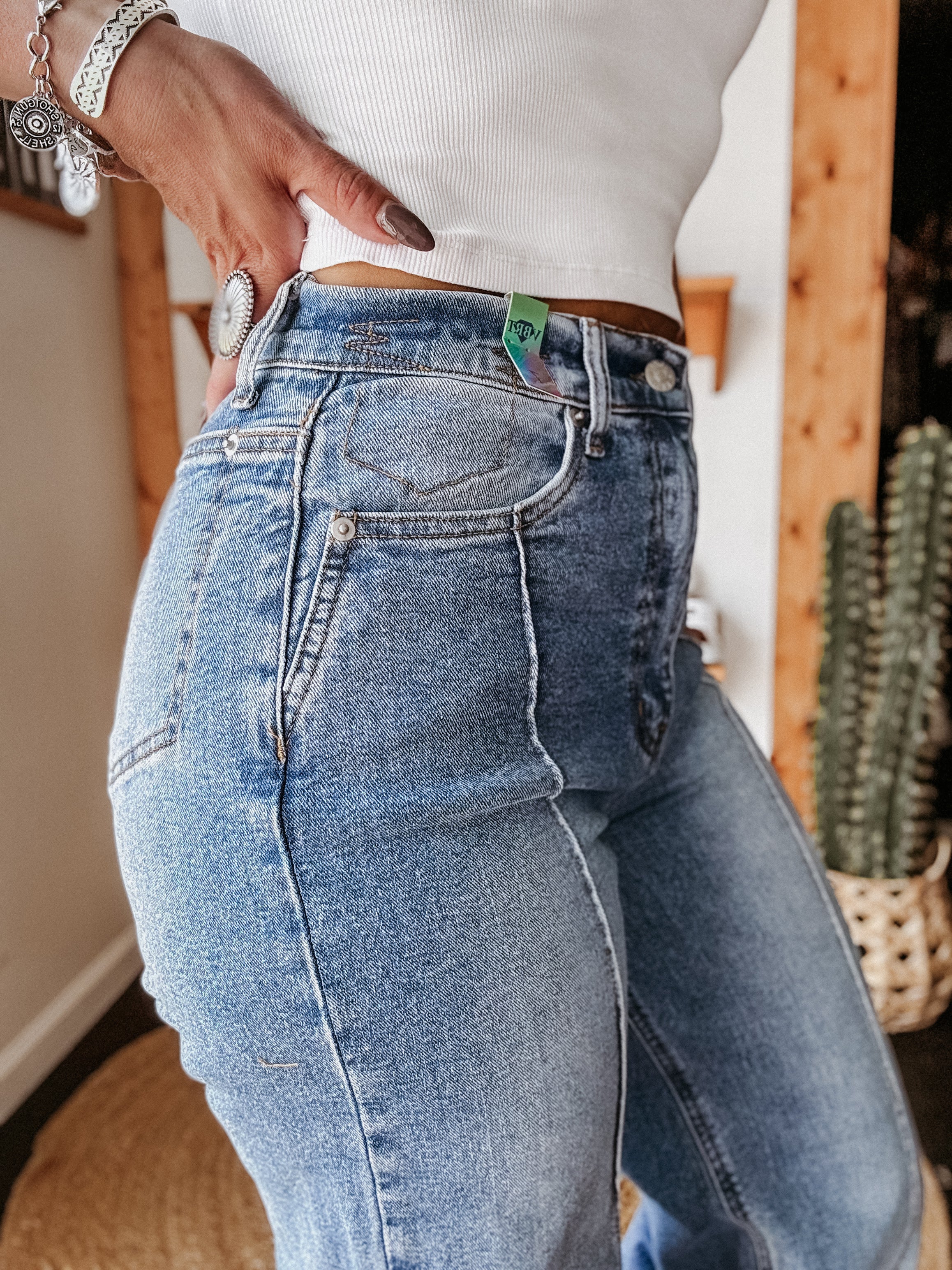 Woman wearing high-waisted blue western jeans and a white ribbed tank top indoors.