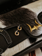 Cow print western leather bag with gold antler detail and small hoop earrings