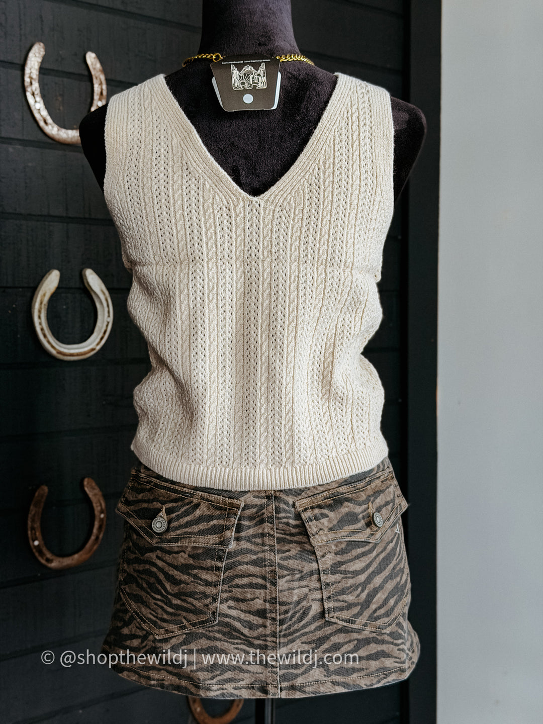 Mannequin wearing a cream sweater vest and zebra print shorts against a dark background with horseshoes.