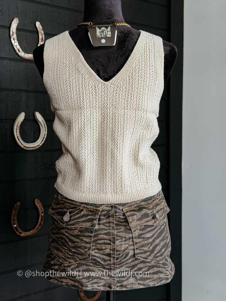 Mannequin wearing a cream sweater vest and zebra print shorts against a dark background with horseshoes.