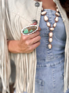 Woman in western fringe jacket and denim holding large turquoise statement ring