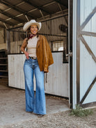 Woman in a cowgirl hat, suede jacket, high-waisted flare jeans, western boho outfit in barn