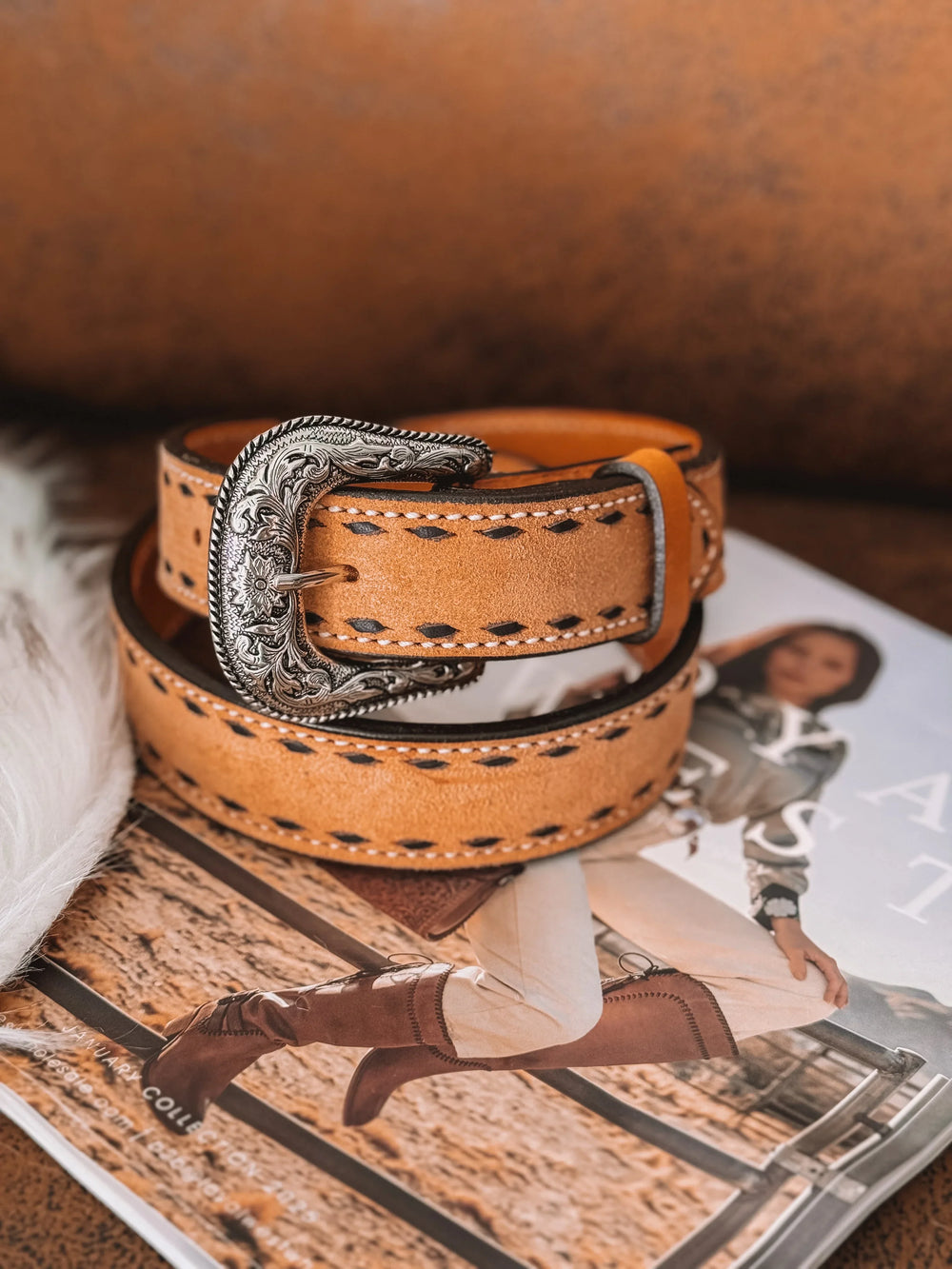 Western tooled leather belt with ornate silver buckle on a magazine featuring cowgirl fashion