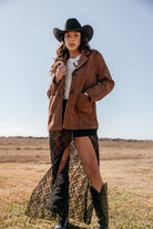 Woman in western outfit with brown suede jacket, black lace skirt, cowboy hat and boots outdoors