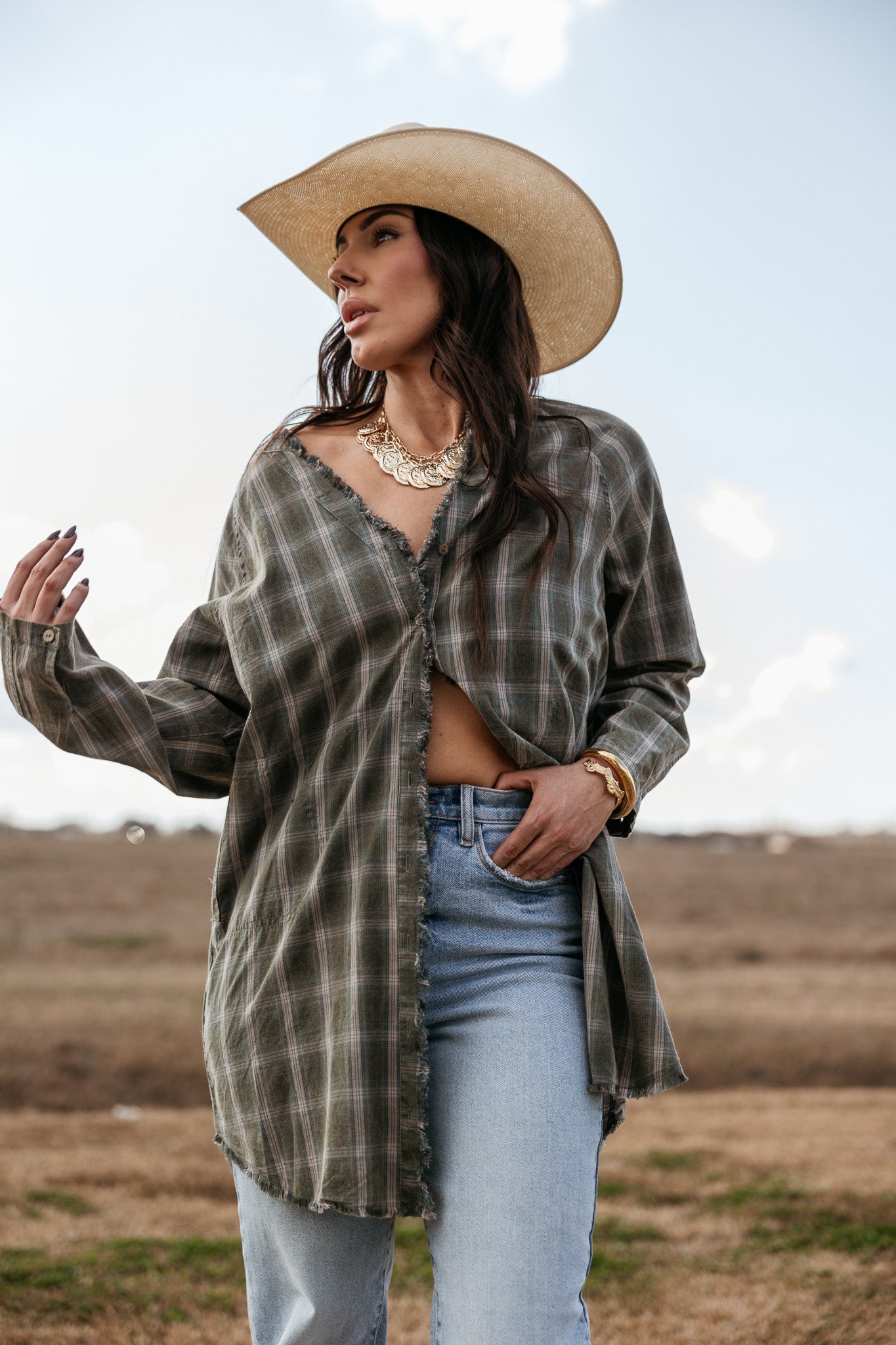 Woman in a straw cowboy hat, plaid western shirt, and distressed jeans outdoors