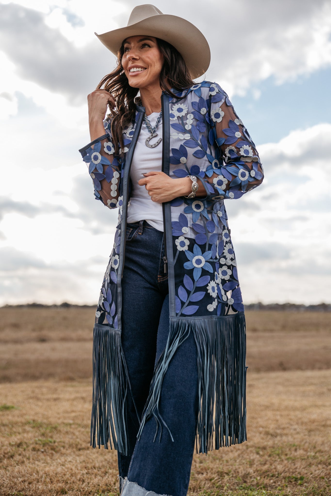 Woman in cowgirl hat wearing blue floral embroidered sheer duster with fringe, western jean outfit