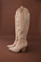 Tan suede western cowgirl boots with embroidery and block heels on brown background