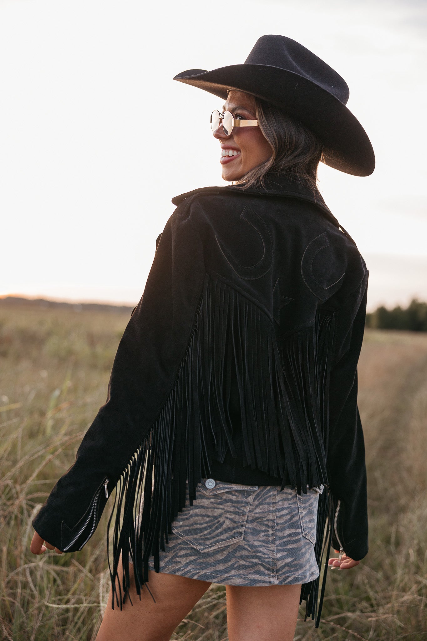 Woman wearing a black fringe jacket and cowboy hat in a field