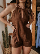 Woman wearing sleeveless brown suede romper, western boho style, with cactus decor