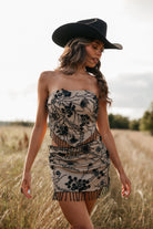 Woman in a strapless embroidered beaded set and black cowboy hat standing in a field.