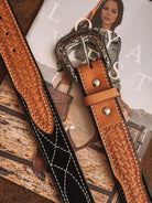 Tooled leather western belts with ornate silver buckle on a magazine featuring western fashion.