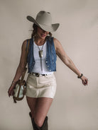 Woman in cowgirl hat, denim vest, white tank, cream mini skirt, and boots, western boho style