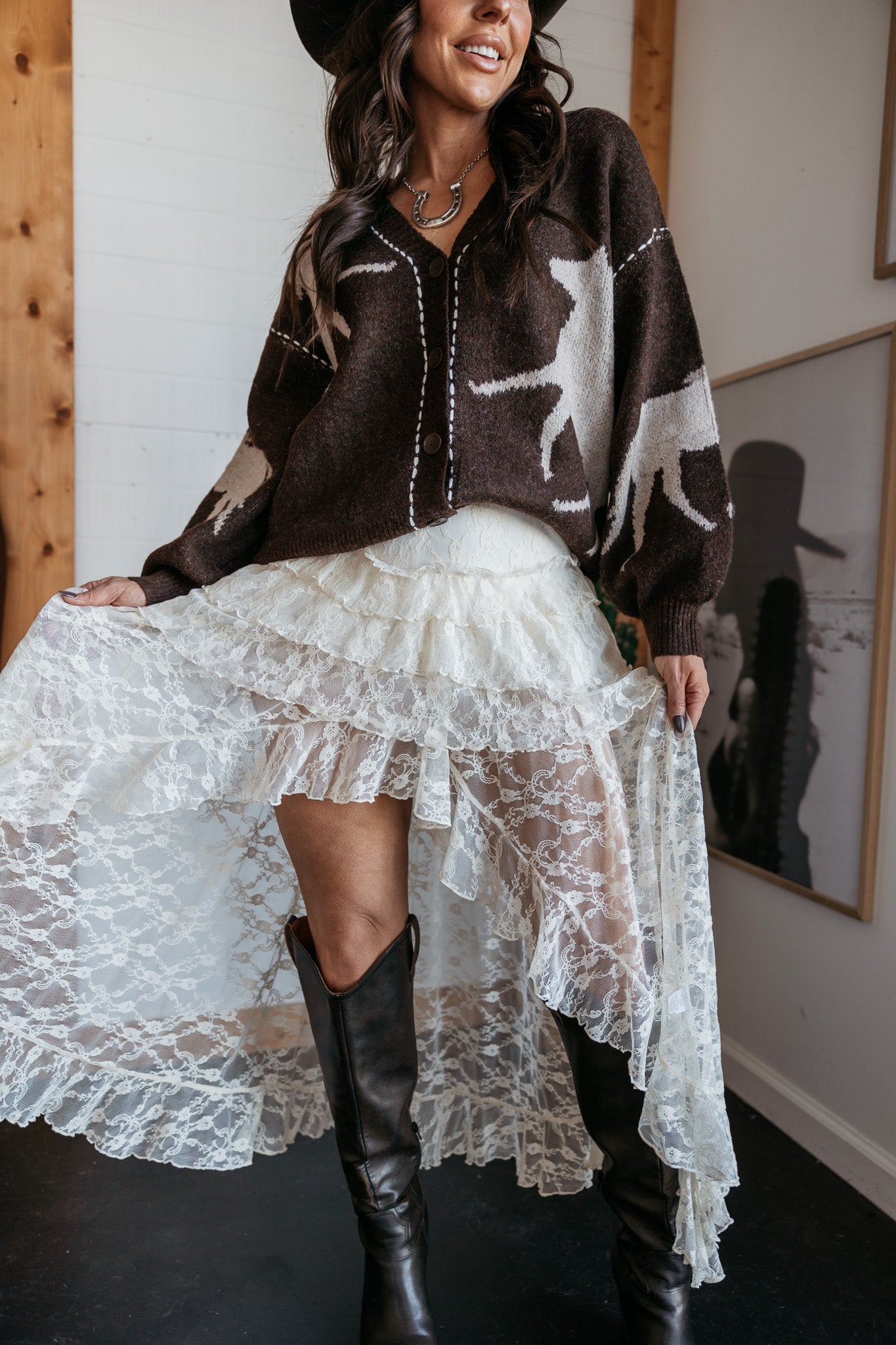 Woman in cowgirl hat, brown western cardigan, lace skirt, black boots, boho western outfit