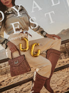 Gold western-style hoop earrings on magazine featuring cowgirl in embroidered shirt, boots, tooled purse.