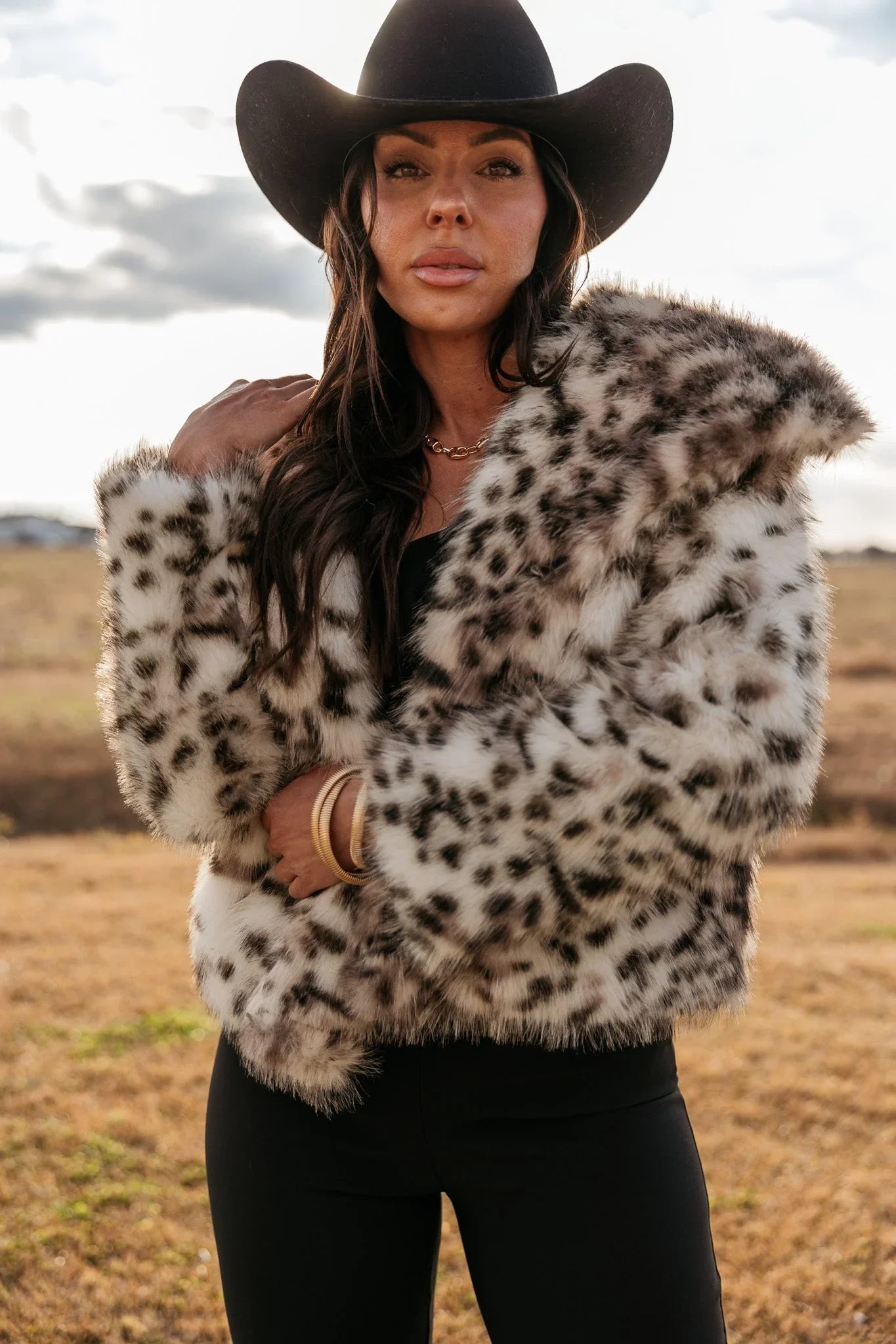 Woman in a western hat and leopard print faux fur jacket outdoors, boho cowgirl fashion
