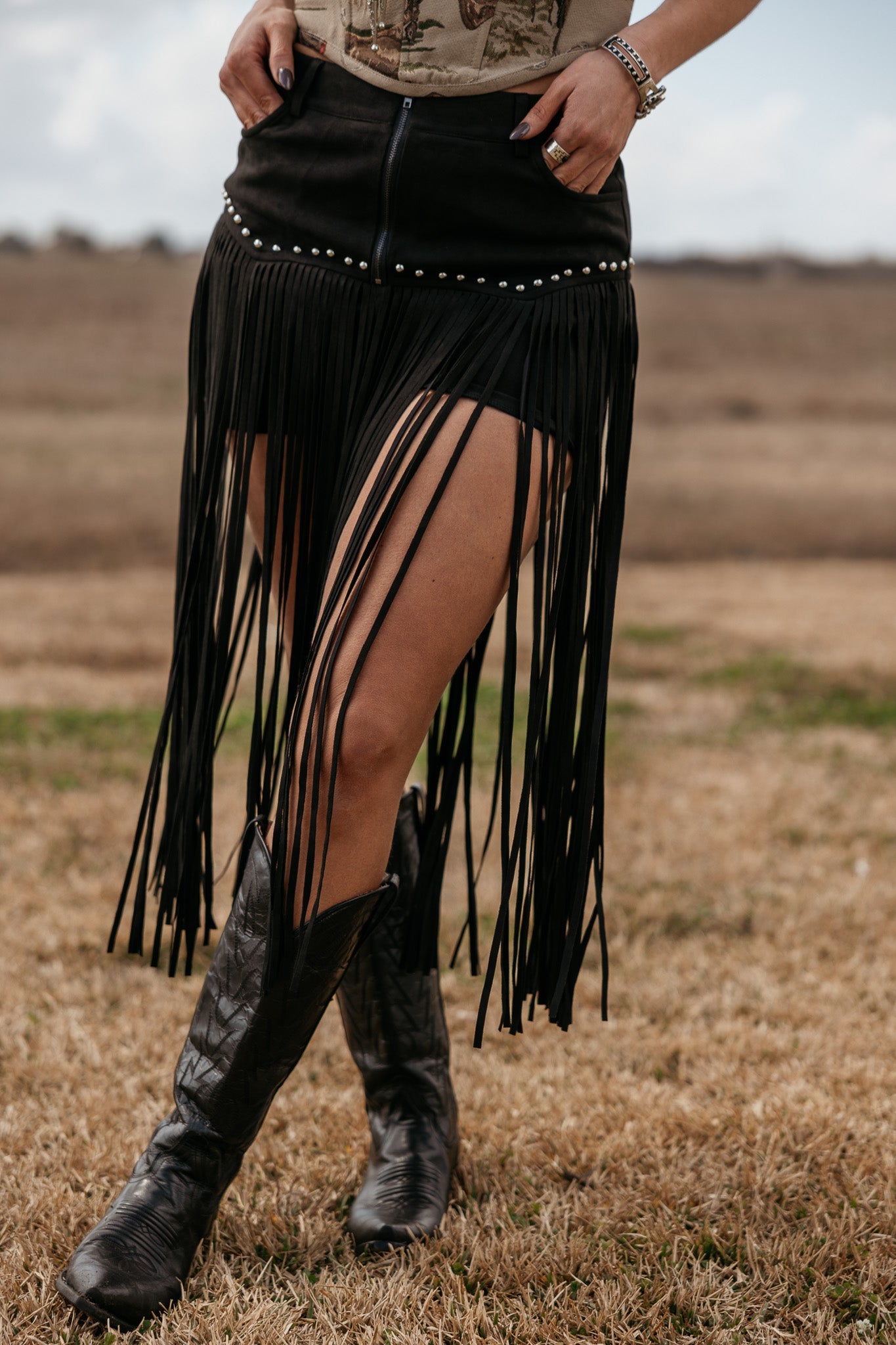 Woman wearing black fringe western skirt and cowboy boots in a rustic outdoor setting