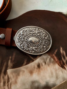 Western engraved silver belt buckle on brown leather strap, cowgirl accessory closeup