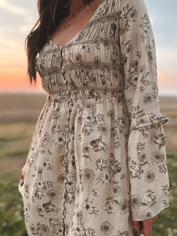 western boho dress in white with sage floral print with a slit and beige knee-high cowgirl boots close up. model in field