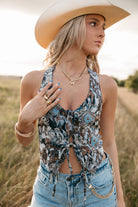 Woman wearing a patterned top and denim shorts with a cowboy hat in a field.