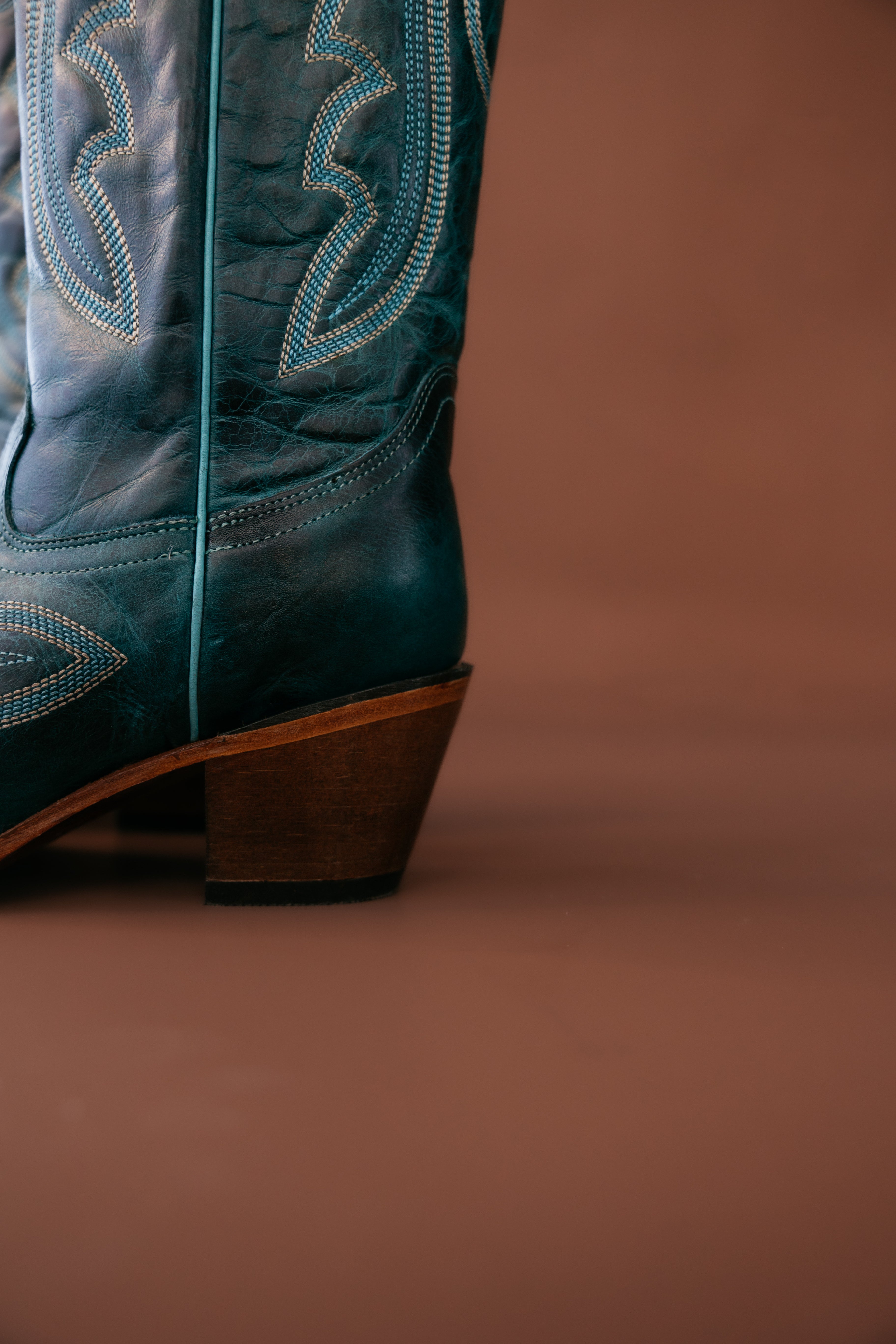 Close-up of teal western cowgirl boot with stitching, brown background, boho style