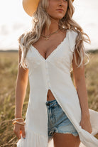 Woman wearing a white sleeveless top with ruffles and denim shorts in a field.