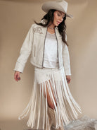 Woman in western boho outfit with white fringe skirt, embroidered jacket, cowboy hat and boots