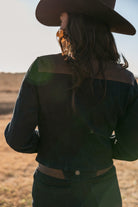 Woman in dark denim western jacket and cowboy hat, outdoors in sunlight, boho cowgirl style
