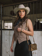 Woman in western cowgirl outfit with white hat, gingham vest, and suede purse in barn setting