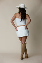 Woman in white cowboy hat, white tube top, white mini skirt, and tan western boots