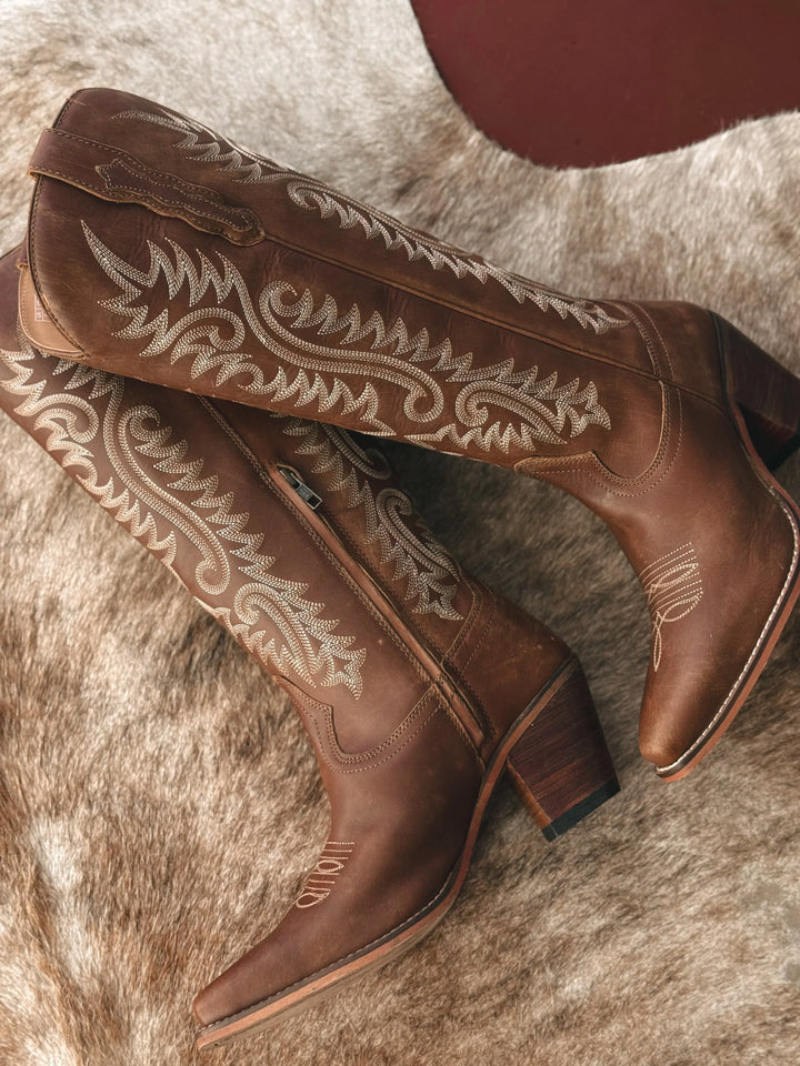 Brown cowboy boots with intricate white embroidery on a fur surface