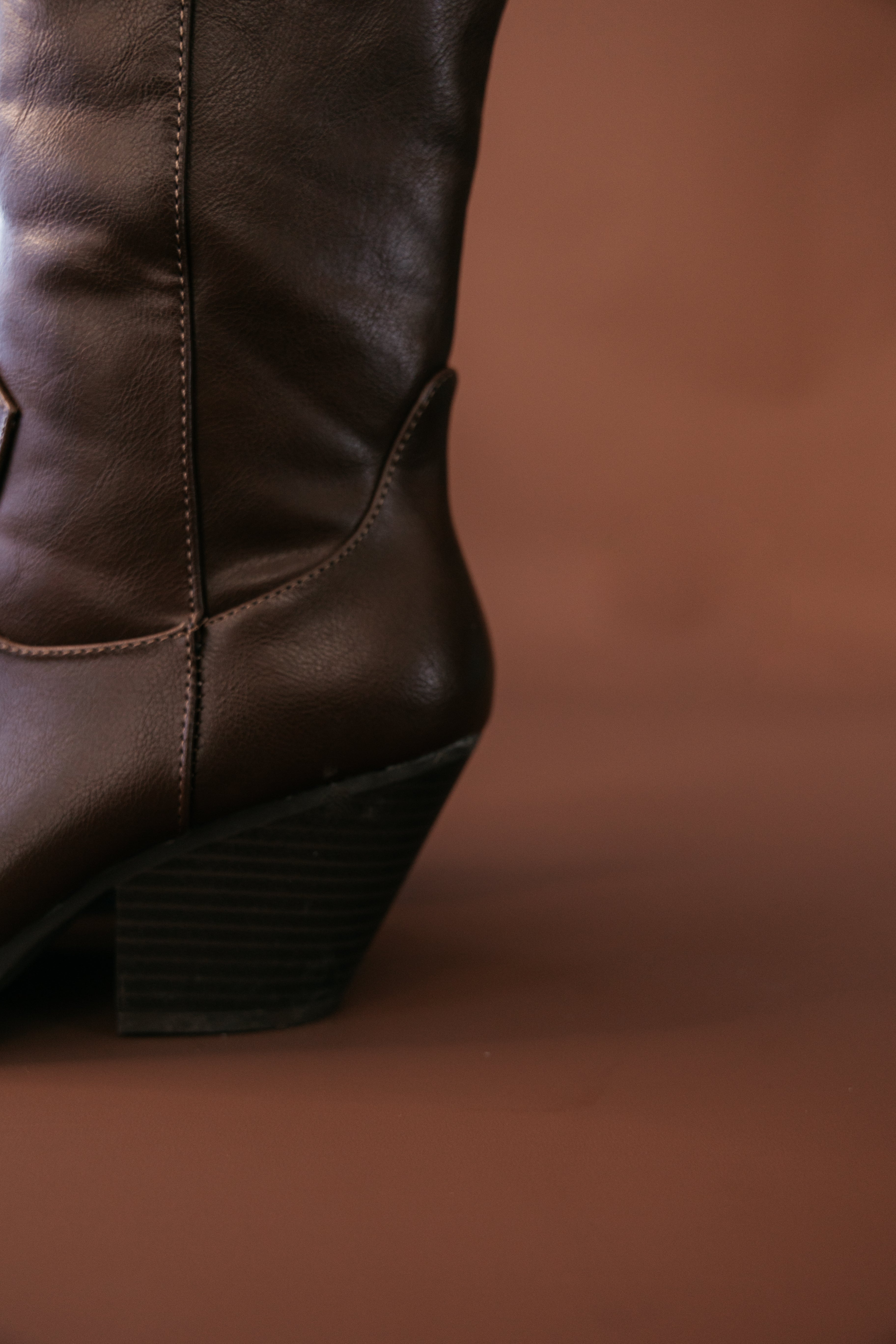 Close-up of brown leather western cowgirl boot with stacked heel on brown background