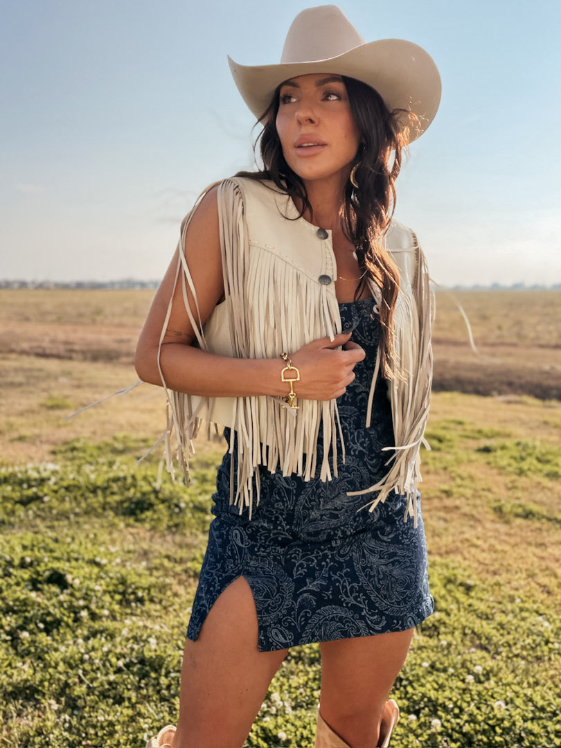 Woman wearing a fringe vest and cowboy hat in an open field