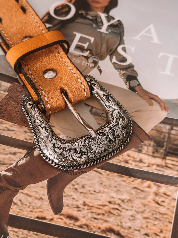 Tooled western leather belt with ornate silver buckle on magazine with cowgirl fashion.