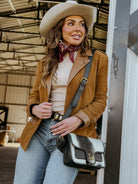 Woman in western boho outfit with tan suede jacket, wide-brim hat, and cow print bag