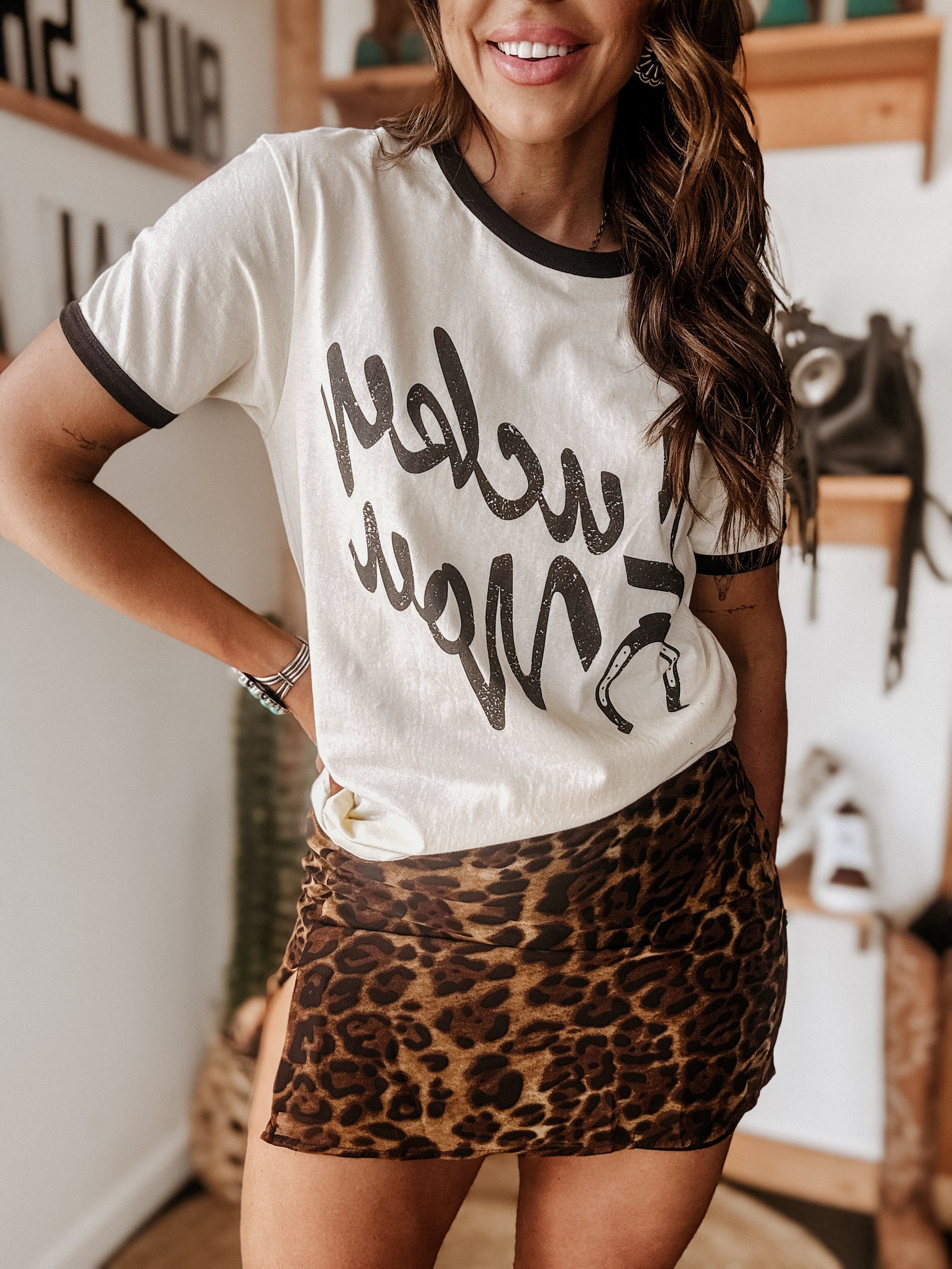 Woman in western graphic tee and leopard print mini skirt in boho boutique setting