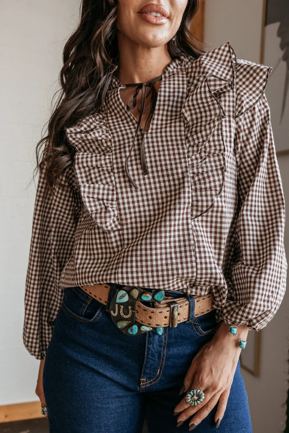 Woman in brown gingham ruffle blouse, turquoise western belt, and denim jeans