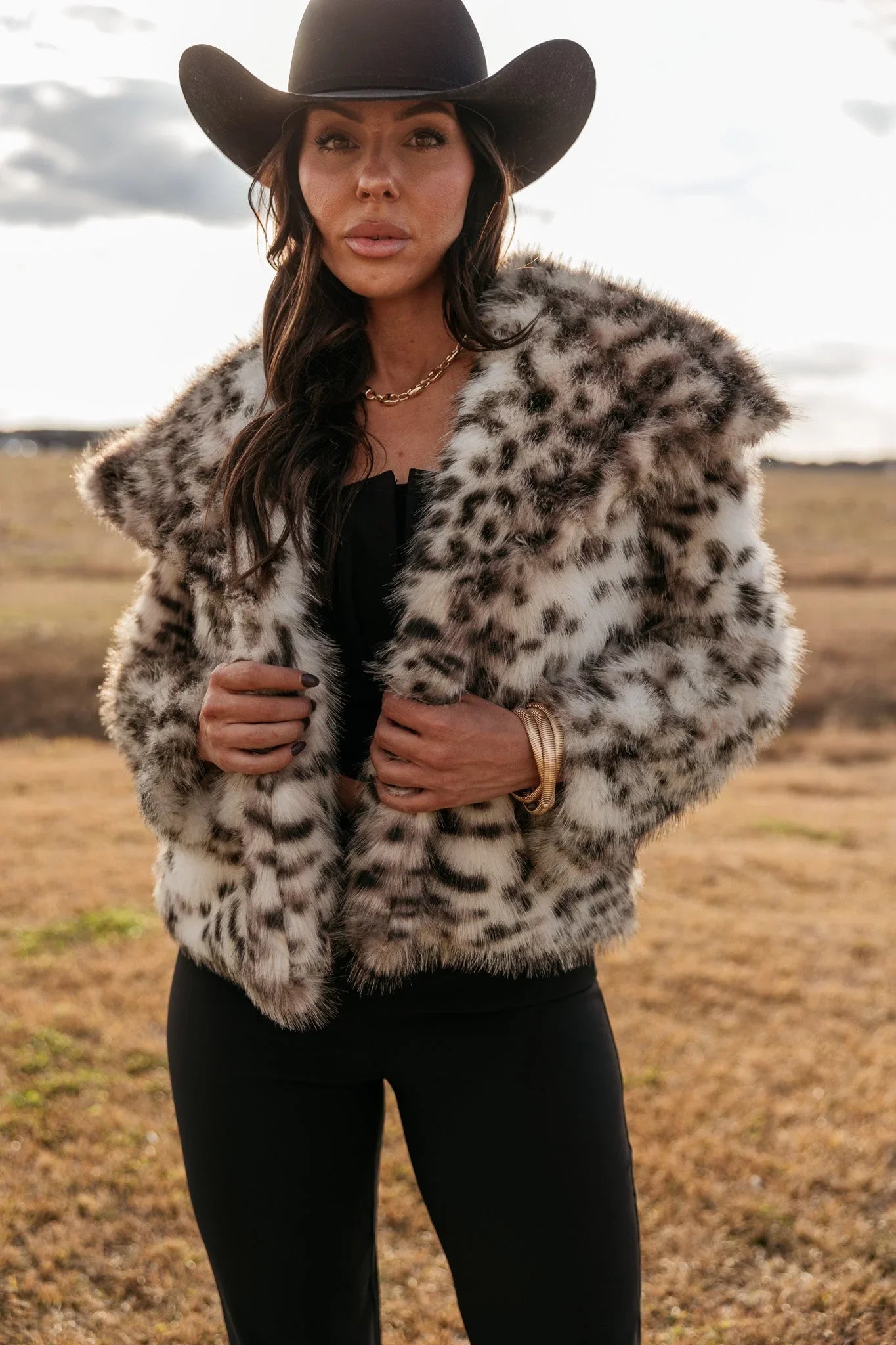 Woman in a black cowboy hat and faux fur leopard print jacket, western boho style outfit outdoors