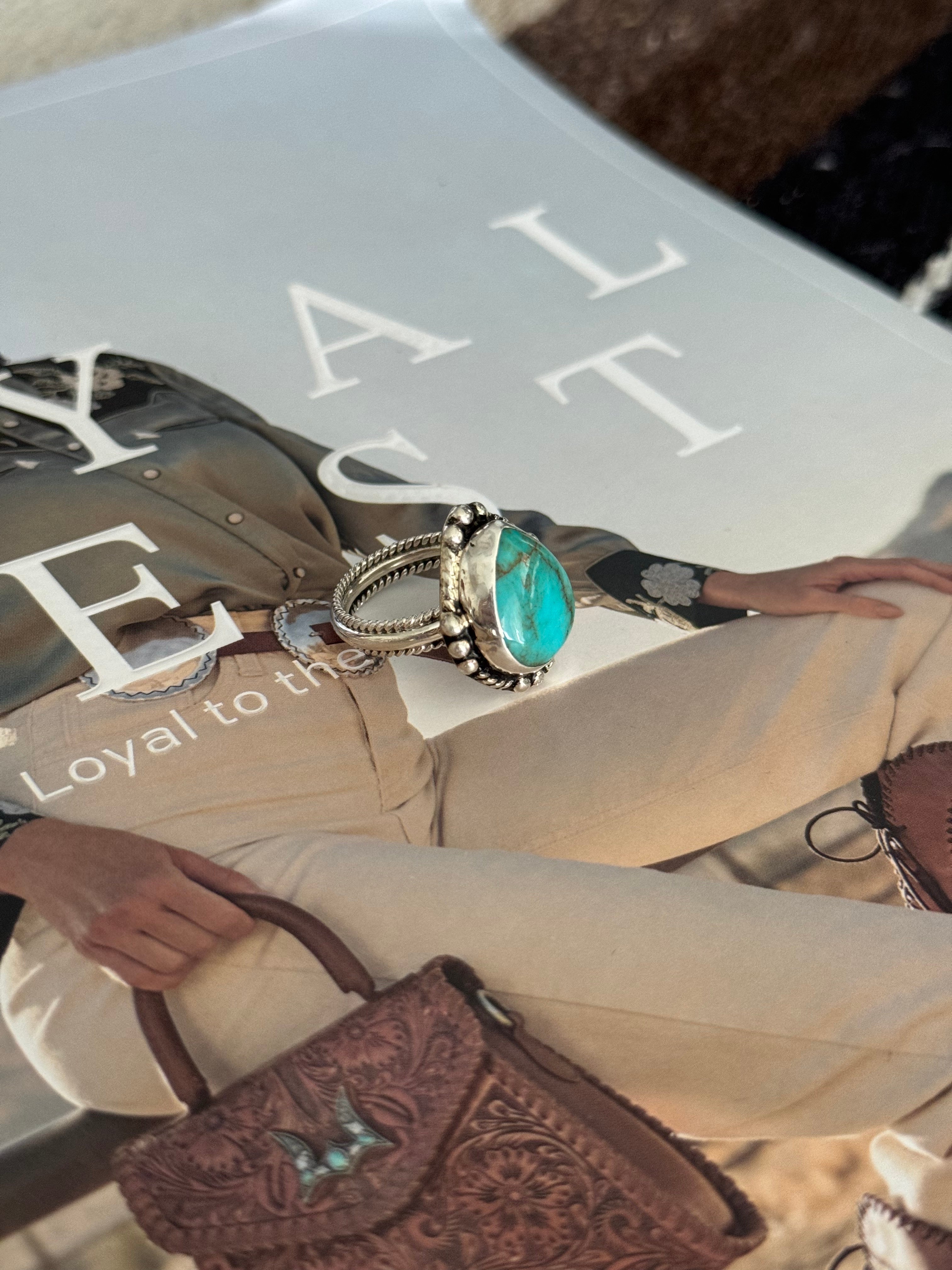 Turquoise western silver ring on cowgirl fashion magazine with tooled leather handbag.