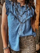 Woman in sleeveless ruffle denim top, leopard print pants, and layered western jewelry